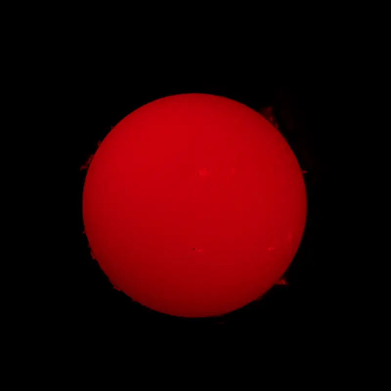 Aurinko punaisena kiekkona H-alfa-aurinkokaukoputkella, reunalla kaasukielekkeitä.