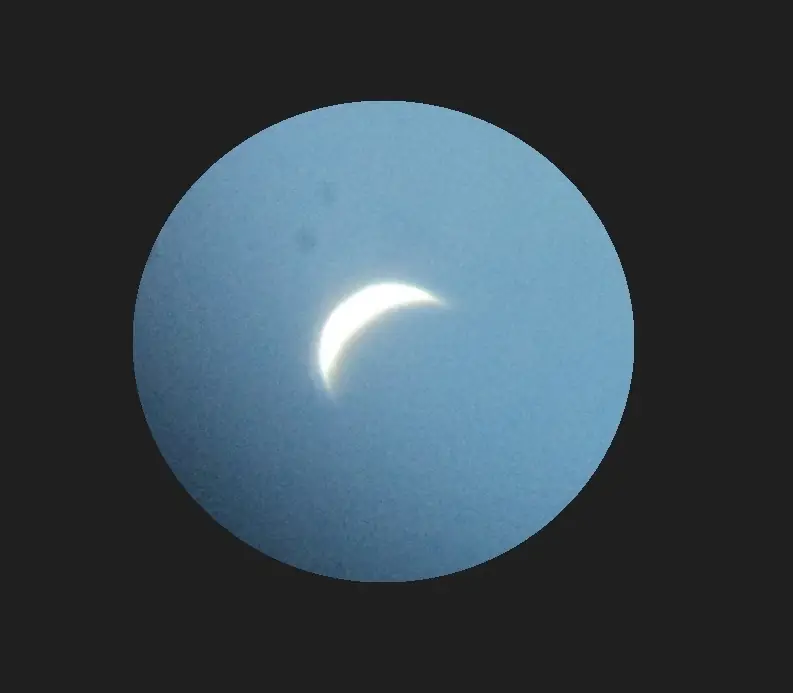 Venus kapeana sirppinä kaukoputken näkökentässä sinistä päivätaivasta vasten.